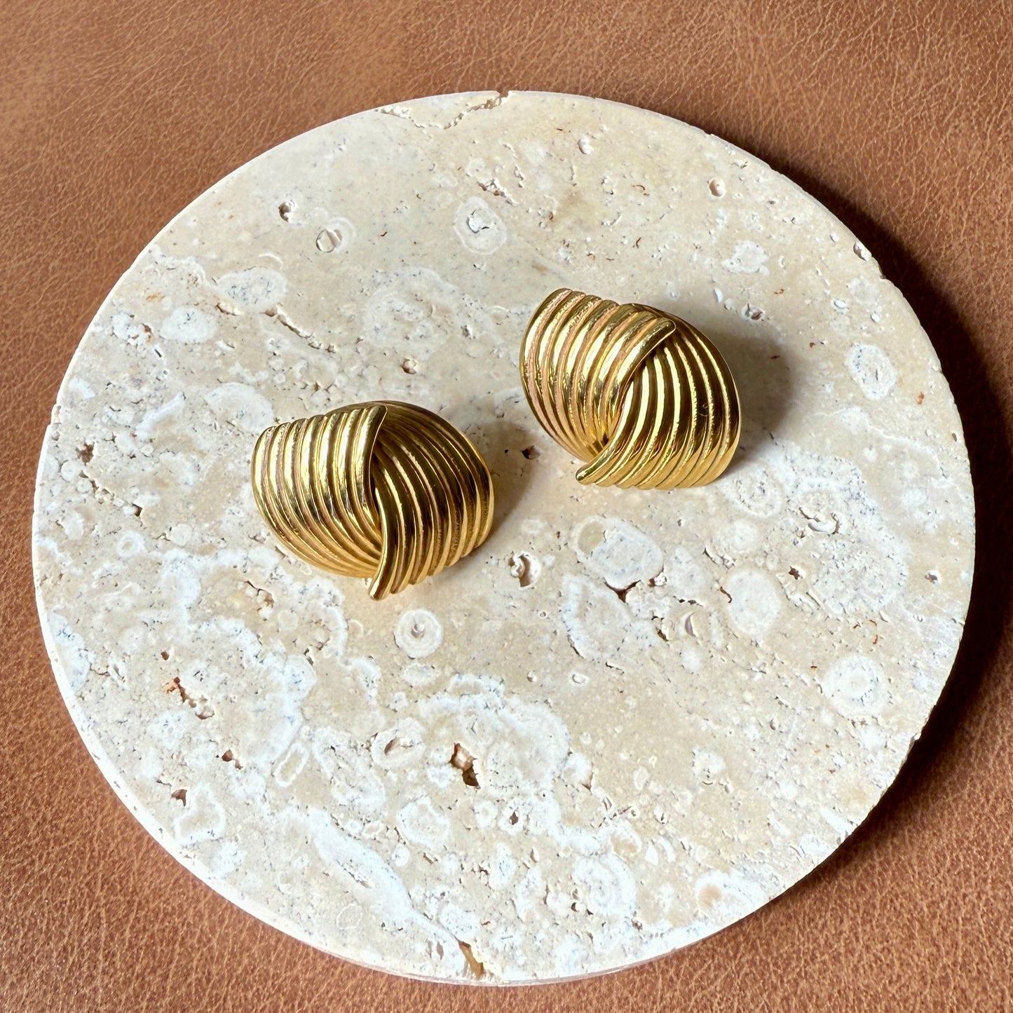 Gold earrings on a round stone coaster with a brown surface