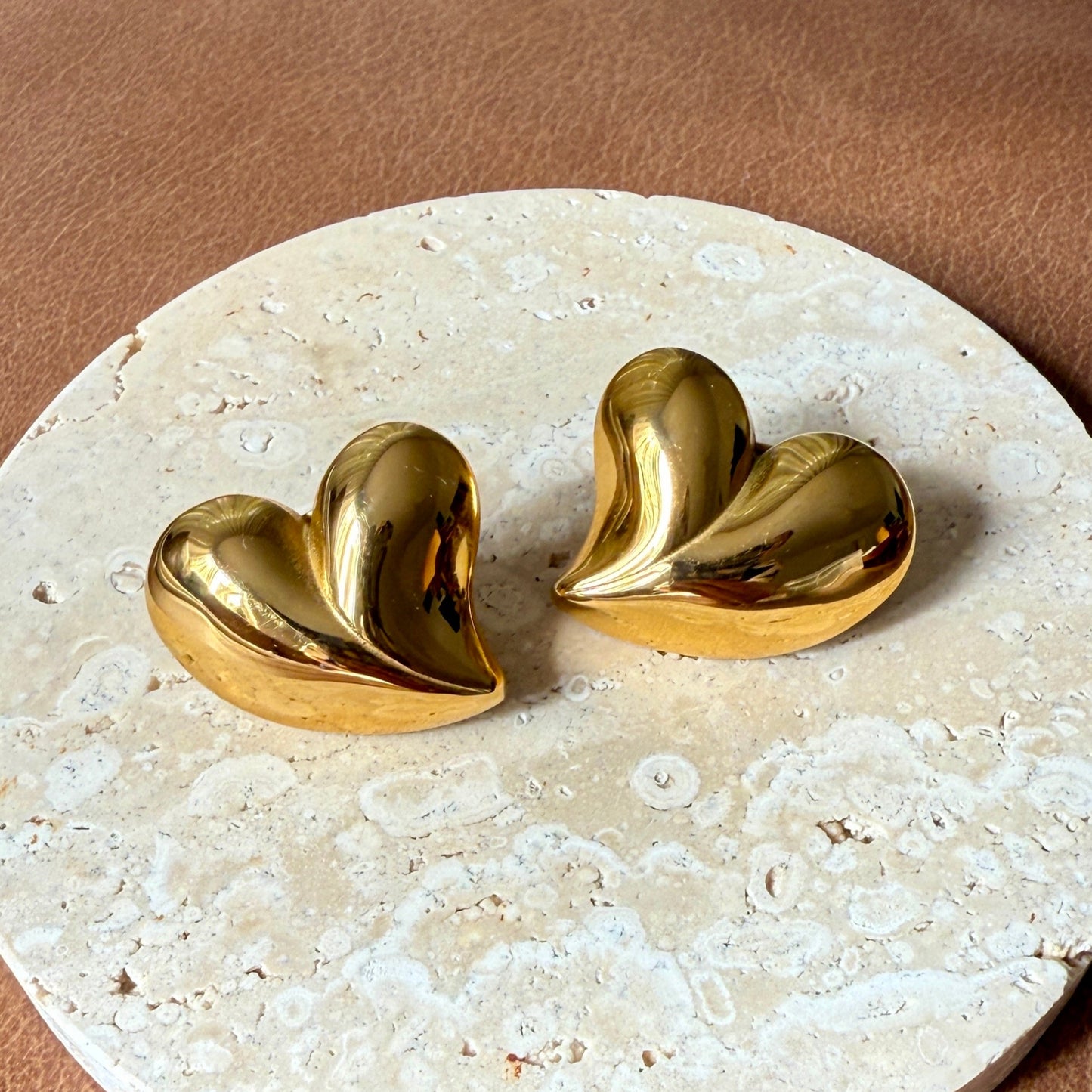 Gold heart-shaped earrings on a round stone surface with a brown background